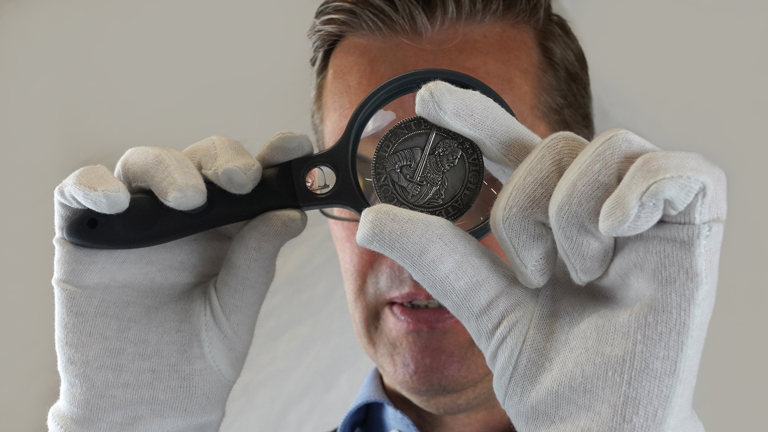 Man onderzoekt muntstuk met vergrootglas.